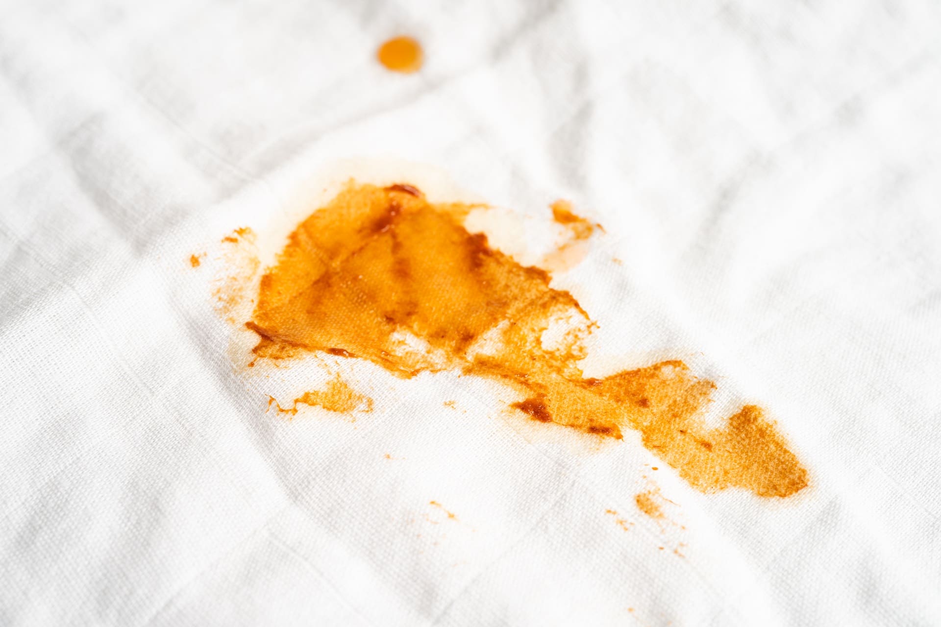 A close-up of a yellow-orange stain on a white fabric surface.